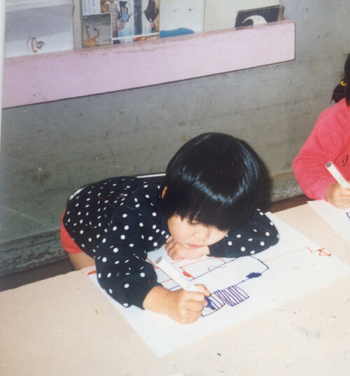 机に向かい白い紙にマジックで絵を描いている幼少時の松橋萌氏